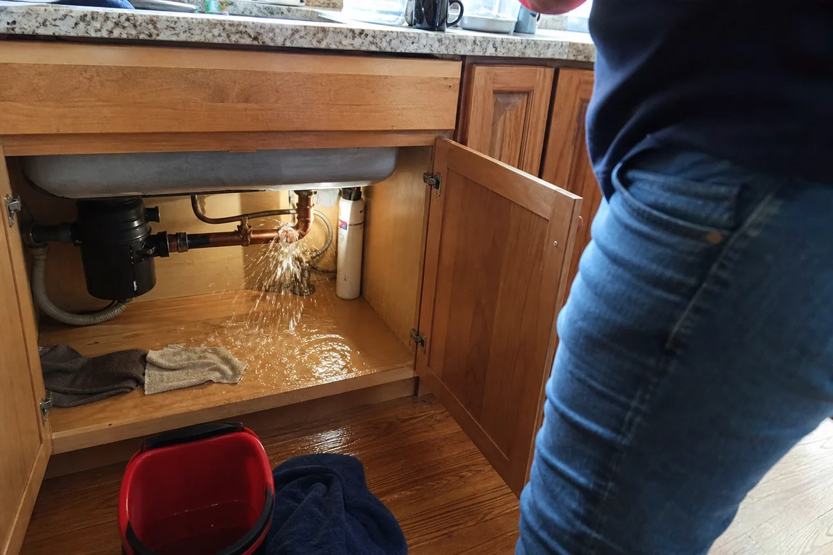 Burst pipe under a sink spraying water
